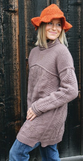 Betsy Wyeth version of New Zealand sweater on young woman, light pink/beige tunic-length with quaker sleeves and collar, model wears and orange brimmed knit hat