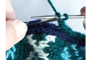 close up of hands working the I-cord buttonhole technique on a piece of blue patterned knitting