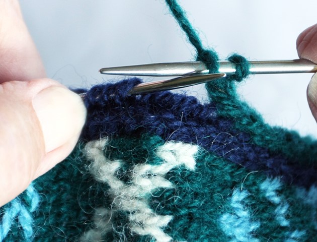 close up of hands working the I-cord buttonhole technique on a piece of blue patterned knitting